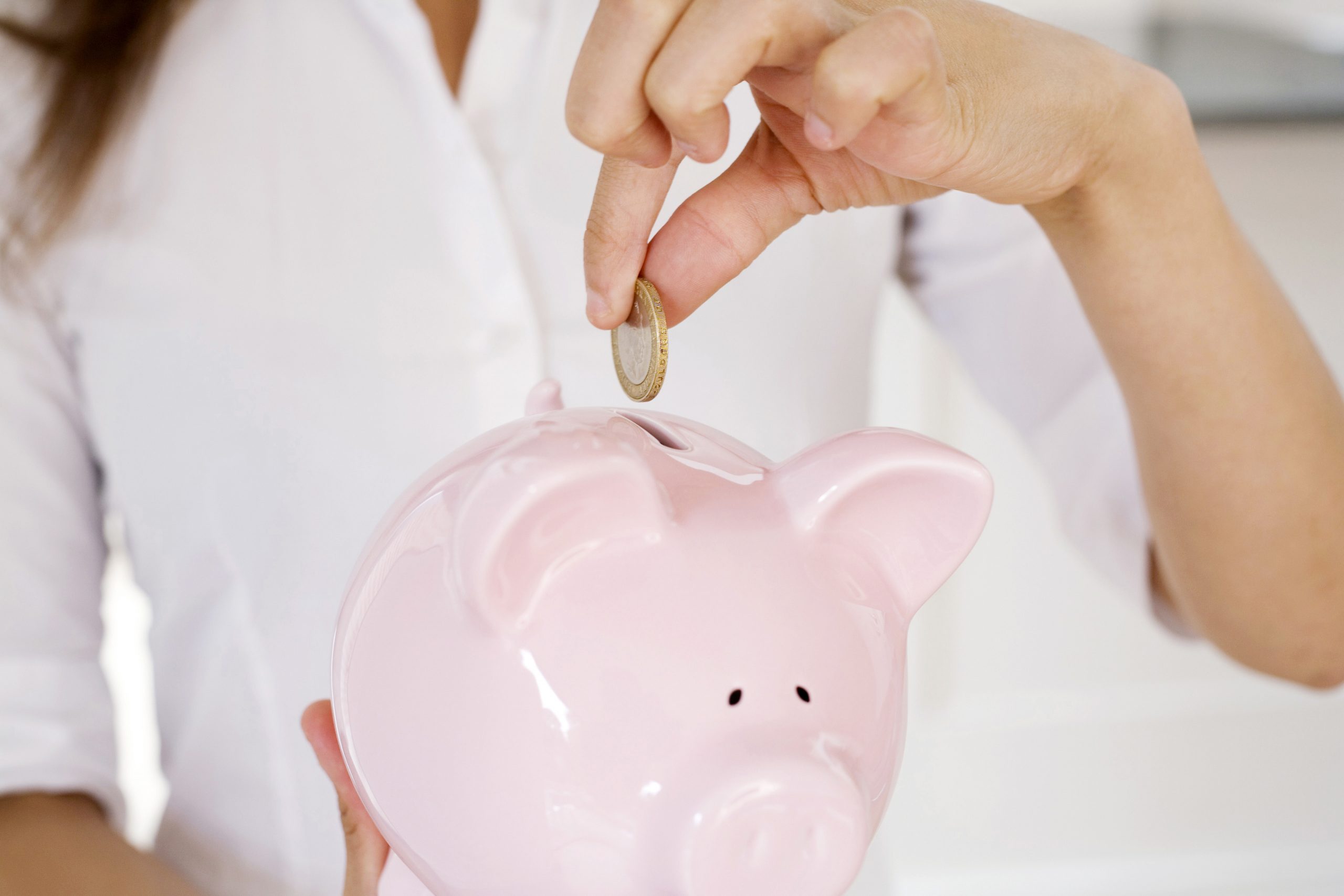 Woman in white shirt putting a coin into a pink piggy bank