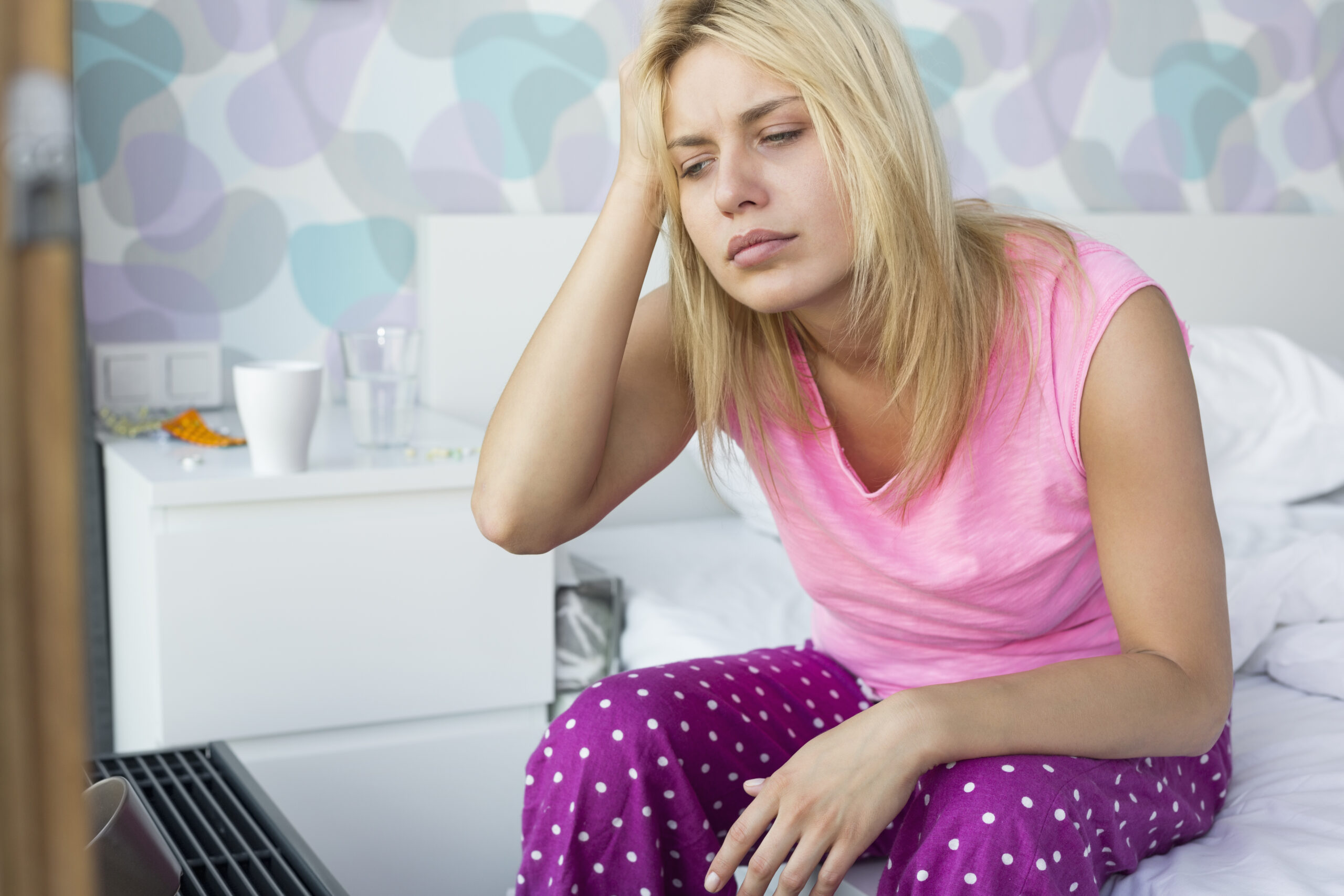 Stressed woman suffering from headache sitting on bed at home