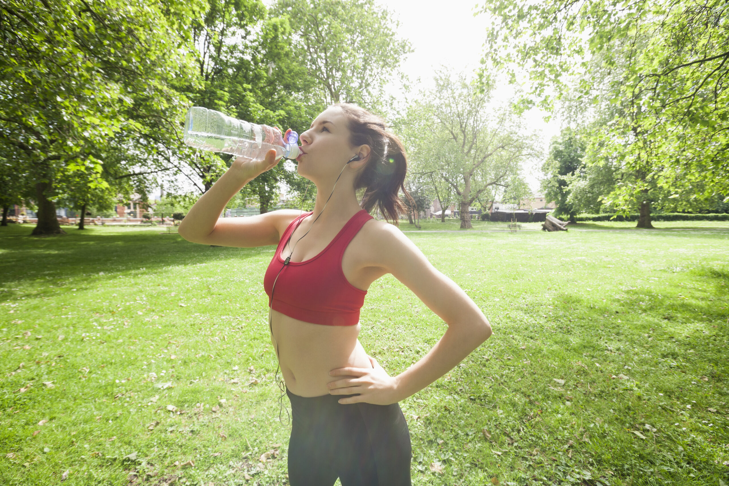 Fit woman drinking water while listening to music in park as she is making healthy lifestyle changes