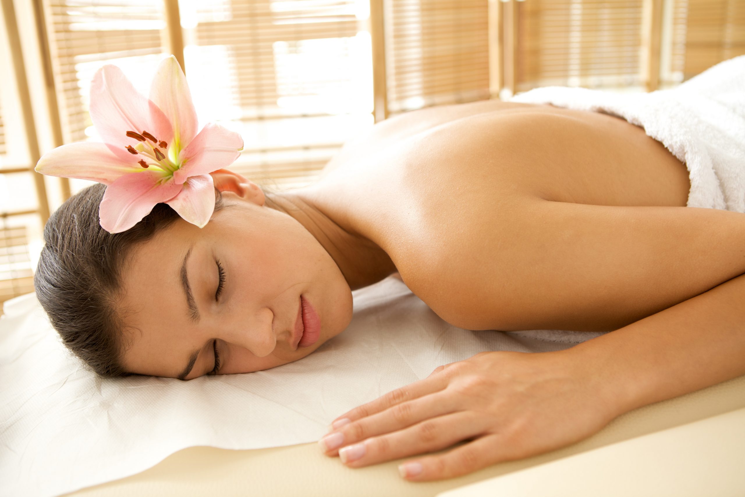 Young woman relaxing on massage table, eyes closed and flower in her hair