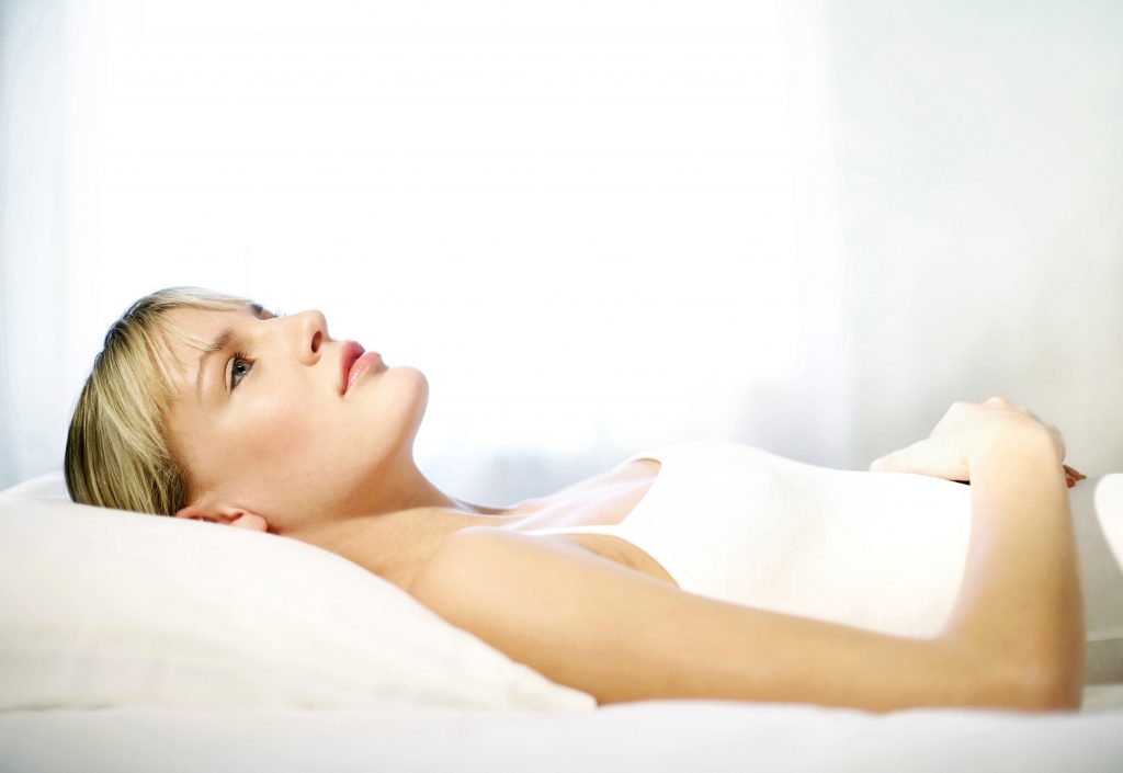 Woman lying down in a white bed looking exhausted