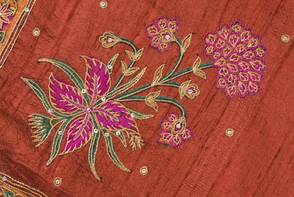 Red silk fabric with pink and gold flowers embroidered on, leaves included in green and gold