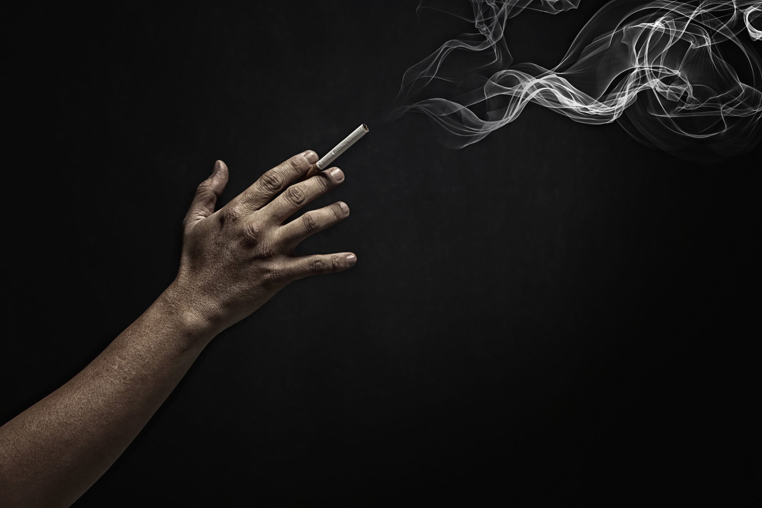 Hand outstretched holding a cigarette with smoke and a dark background