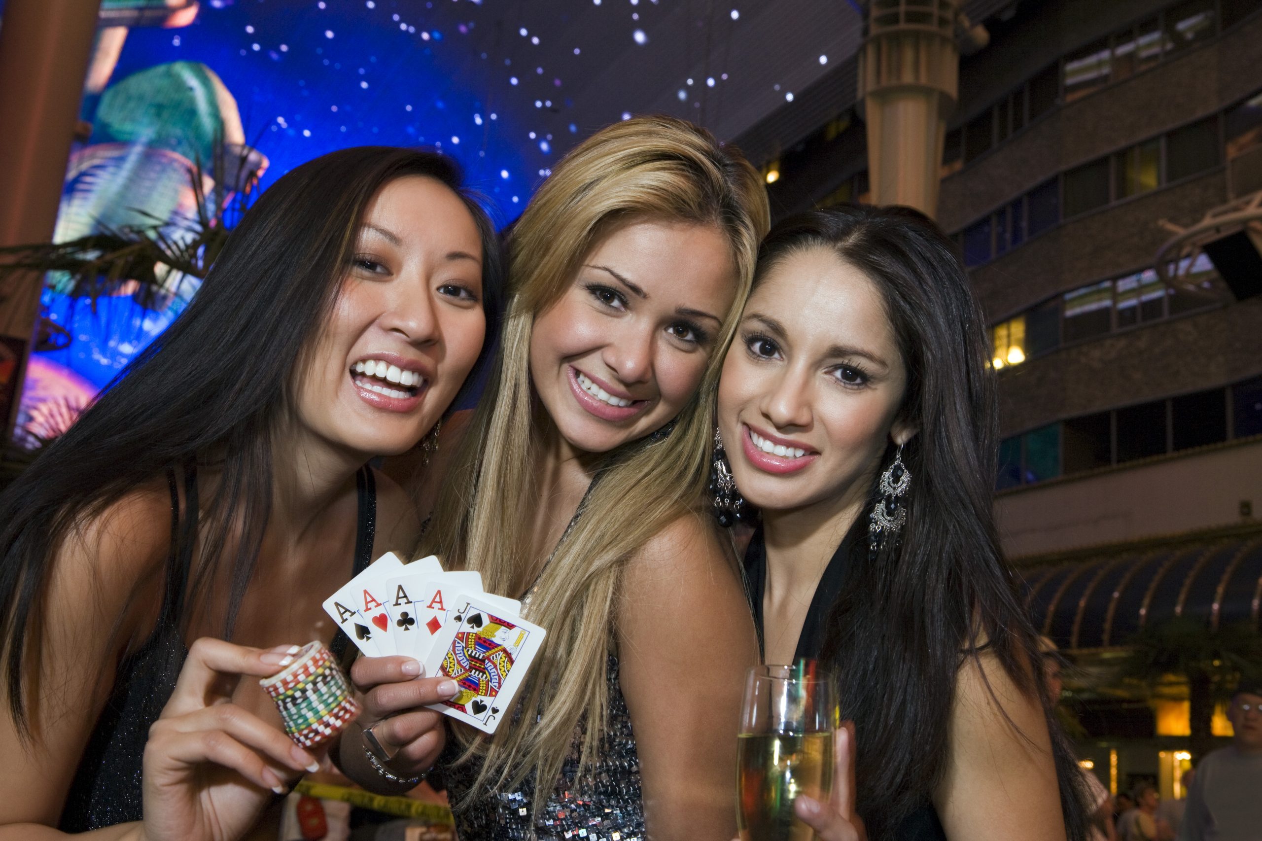 Portrait of three young women with playing cards, gambling chips and champagne in front of casino, Las Vegas, Nevada, USA