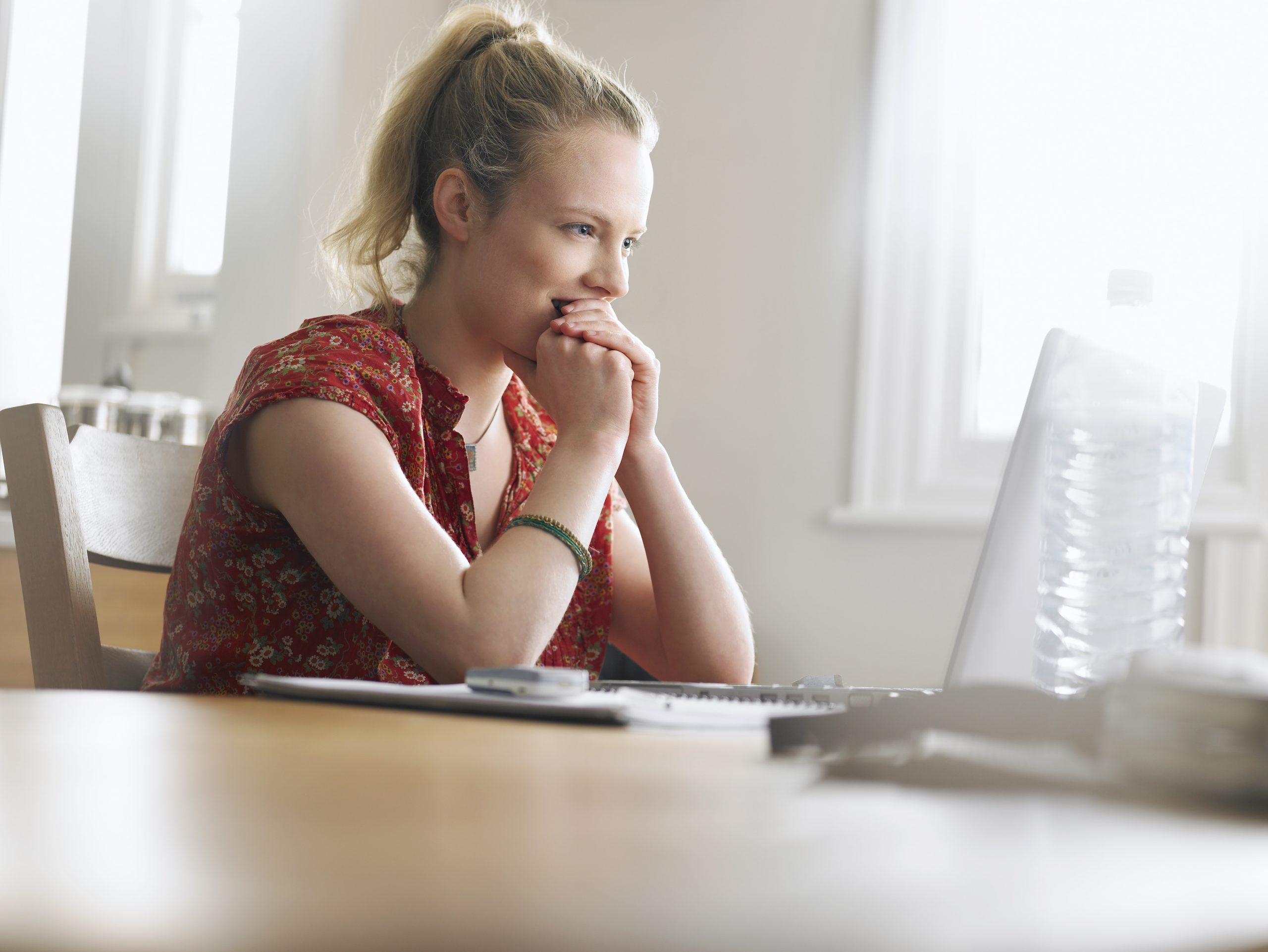 Woman with her chin restong on her hands looking at a laptop screen sat at a table