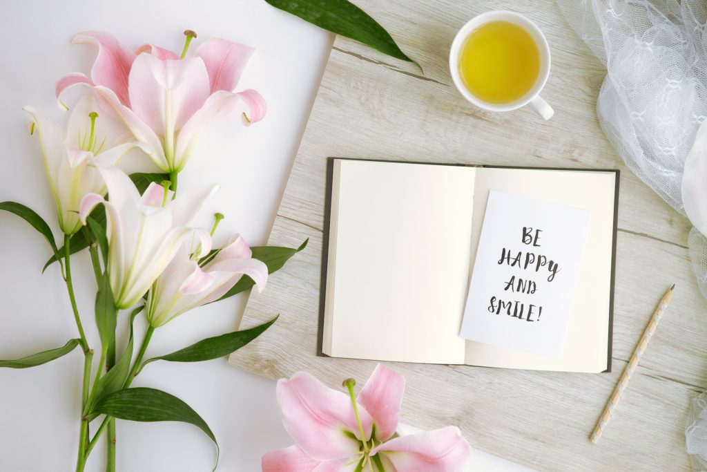 flatlay with a couple of lillies, a book and also a cup of herbal tea