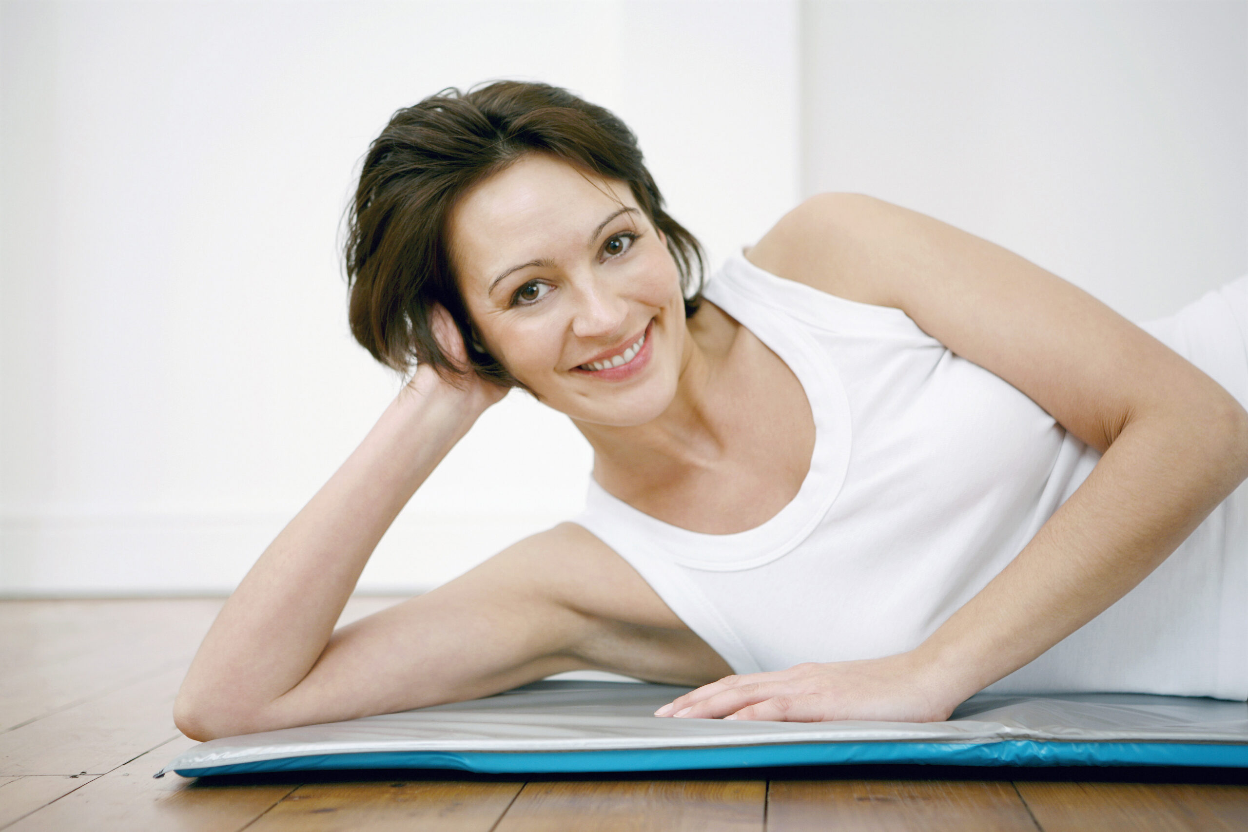 Woman lying down sideways on a yoga mat looking towards the camera, resting head on her hand