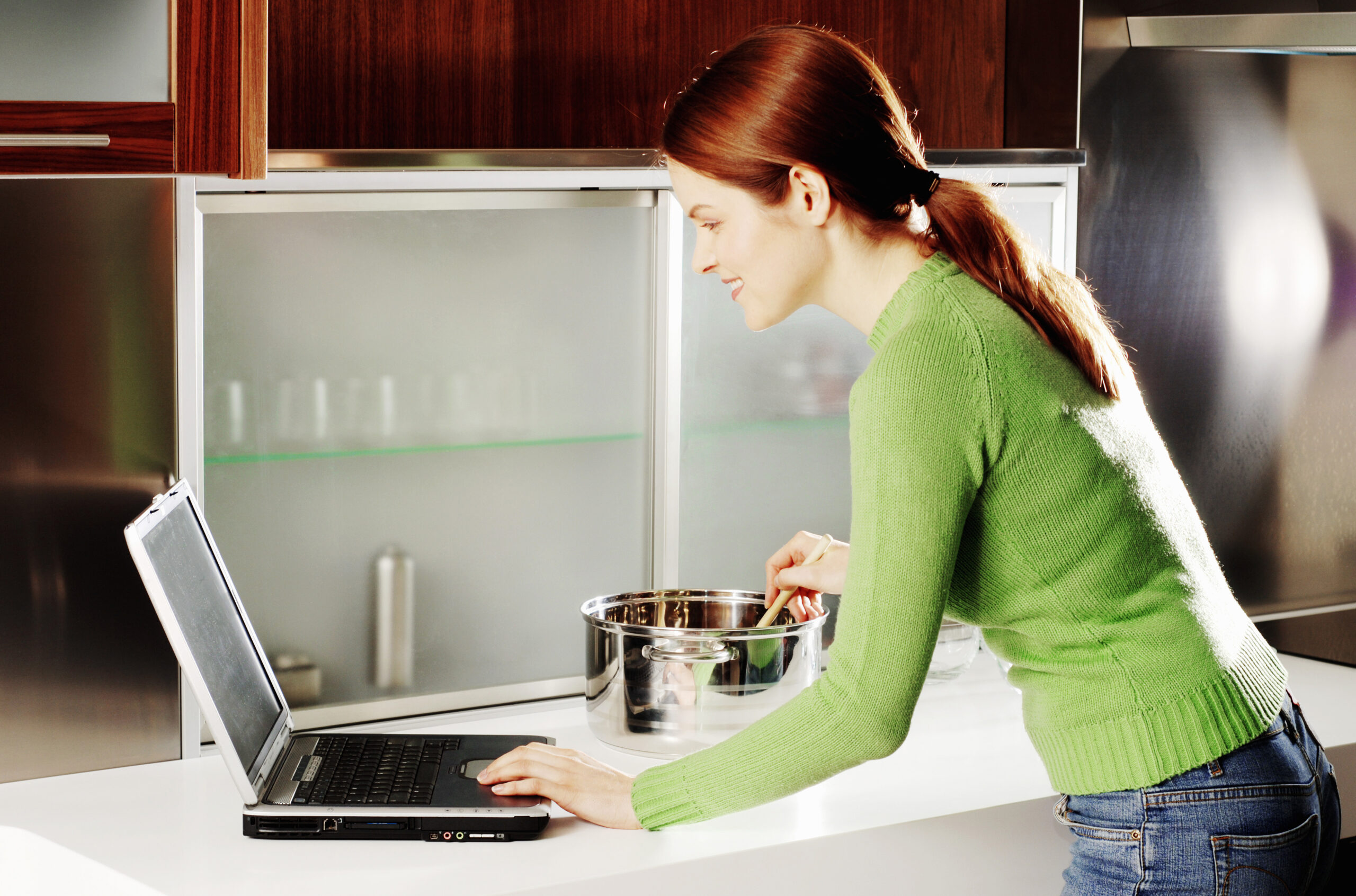 Woman stirring something in a pan whilst using a laptop as they are looking for lockdown love