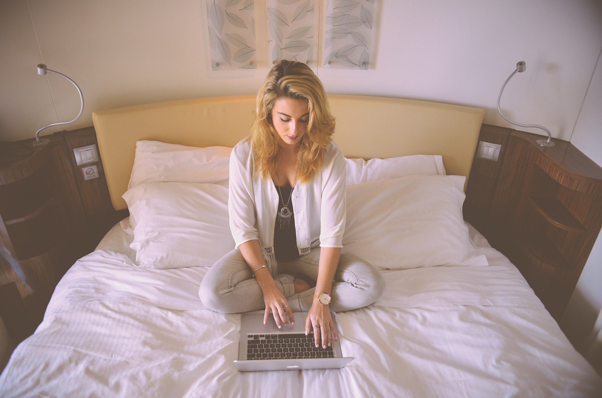 Woman sat in bed with her laptio whilst thinking about Side Hustles To Bump Up Your Income