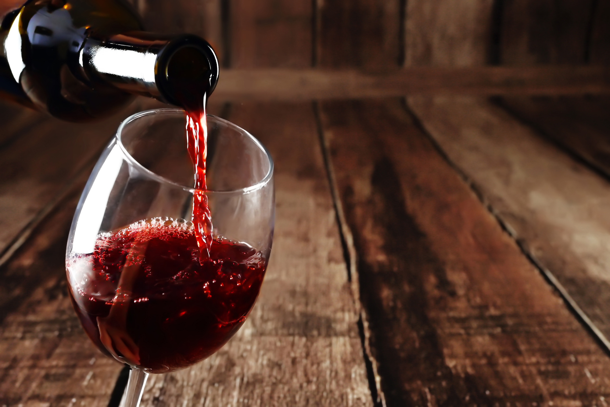 Red wine in glass on wooden background. Beautiful alcohol background. Red wine pouring from bottle. Free space for text on wooden backdrop whilst wine tasting